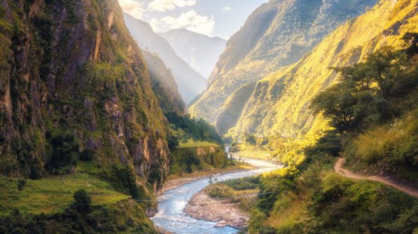 Colorful landscape with high Himalayan mountains, beautiful curving river, green forest, blue sky with clouds and yellow sunlight at sunset in summer in Nepal. Mountain valley. Travel in Himalayas